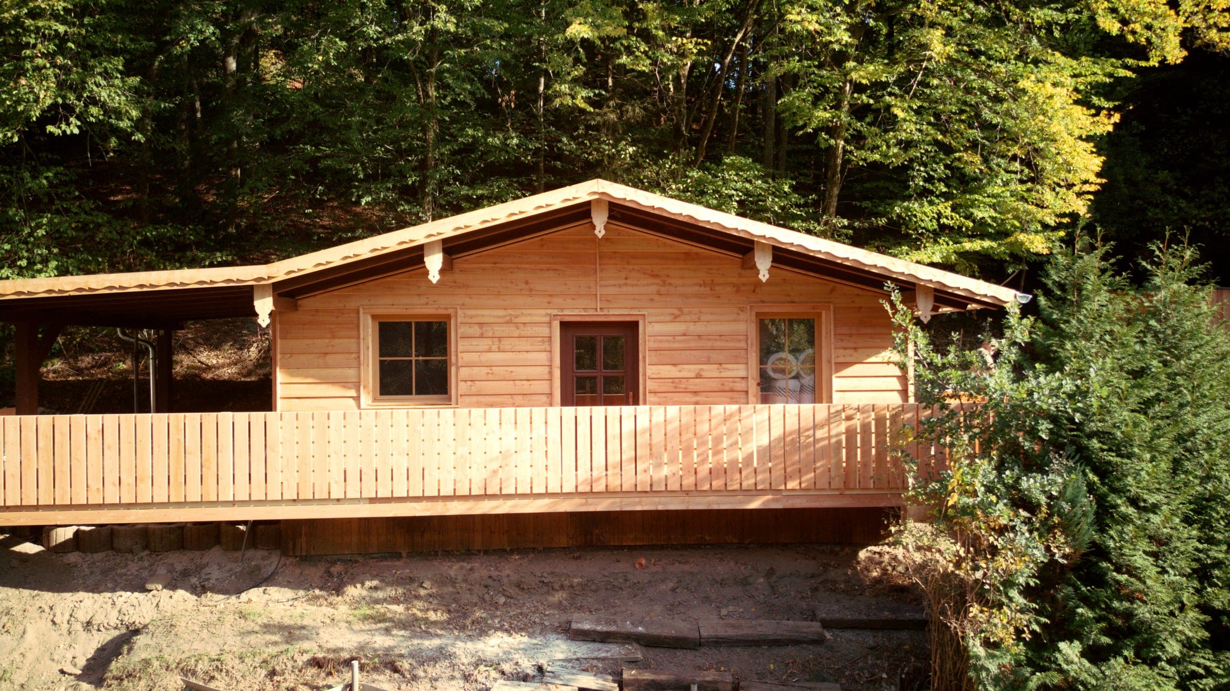 Frontansicht der Holzhütte mit langem Balkon unter goldenen Herbstbäumen bei Thyrnau